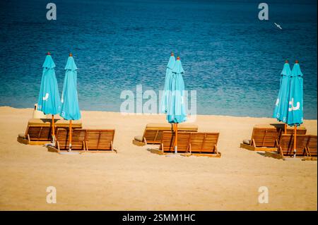 Reihen von bunten Sonnenschirmen und Holzstühlen locken an einem unberührten weißen Sandstrand in Dubai. Perfekt, um die Sonne zu genießen oder am Meer zu entspannen Stockfoto