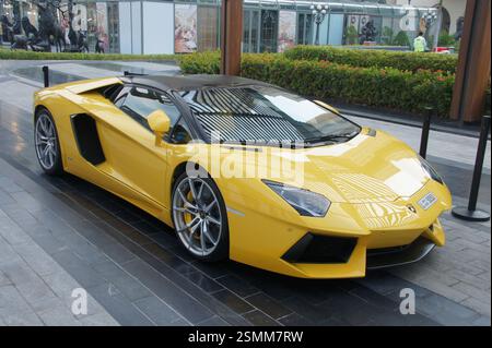 Dubais Stadtbild bietet ein modernes Wunderwerk, während ein eleganter gelber Lamborghini Aventador selbstbewusst vor einem Gebäude mit Glaswänden parkt. Die Schere tut es Stockfoto