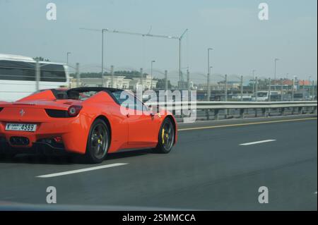 Ein roter Ferrari 458 Spider reißt einen Dubai Highway herunter. Der schlanke Sportwagen verkörpert die Freiheit der offenen Straße, eine aufregende, schnelle Fahrt in einem Traumspiel Stockfoto