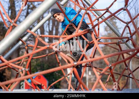 Ein Kind klettert am Frühlingstag in einem Park auf einem Spielplatz auf ein alpines Gitter Stockfoto