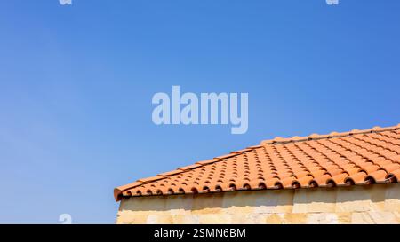 Die Dachziegel des Gebäudes haben einen Hintergrund des blauen Himmels von hellem Himmel, Ton Fliesen Dach, Banner mit orange Ton Fliesen Dach nah oben auf blauem Himmel b Stockfoto
