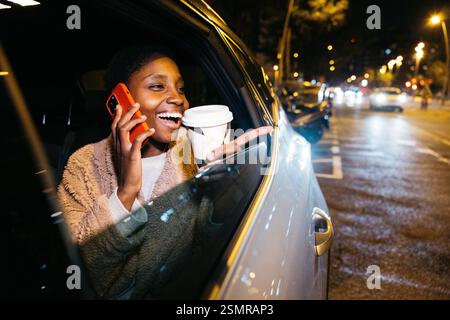 Junge Passagierin, die am Handy spricht und nachts den Finger aus dem Autofenster in der Stadt zeigt Stockfoto