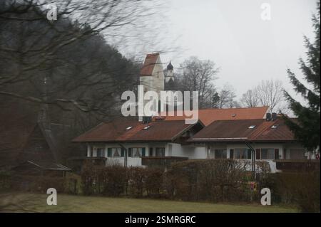 Bunte Häuser säumen eine Straße in Deutschland, München. Ein Uhrenturm blickt über die Dächer in der Ferne. Gepflegte Rasenflächen und Bäume umranden die Häuser Stockfoto