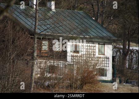 Deutschland, München. Ein weißes Haus mit einem grünen Metalldach liegt eingebettet in einen bewaldeten Bereich. Die friedliche Lage lässt ein charmantes Ferienhaus vermuten, ein Perfec Stockfoto