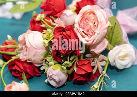 Eine farbenfrohe Kollektion künstlicher Rosen in Rot- und Rosa-Tönen ist elegant auf einer Tischdecke in blaugrün angeordnet und zeigt komplizierte Details und Realis Stockfoto