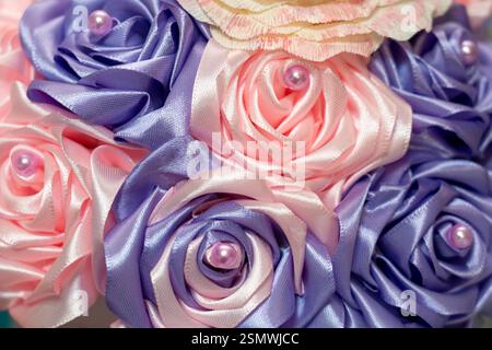 Ein lebhaftes Arrangement aus handgefertigten Satinrosen in Rosa- und Lavendeltönen, verziert mit dekorativen Perlen, die die komplizierte Handwerkskunst und die kunstvolle Handwerkskunst zum Ausdruck bringen Stockfoto