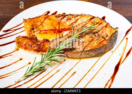 Ein wunderschön überzogenes gegrilltes Lachsfilet, garniert mit frischem Rosmarin und einer Balsamico-Glasur. Das Gericht wird auf einem weißen Teller serviert, Showcas Stockfoto