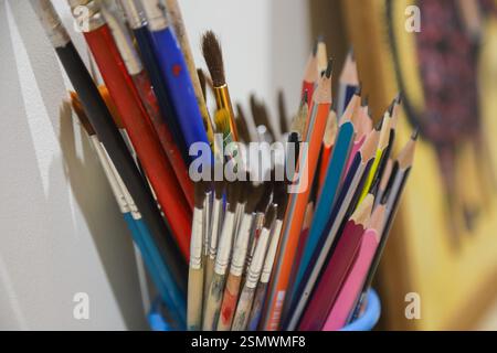 Ein lebhaftes Sortiment an Pinseln und Buntstiften füllt einen blauen Behälter und zeigt die Werkzeuge der Kreativität im Arbeitsbereich eines Künstlers. Stockfoto