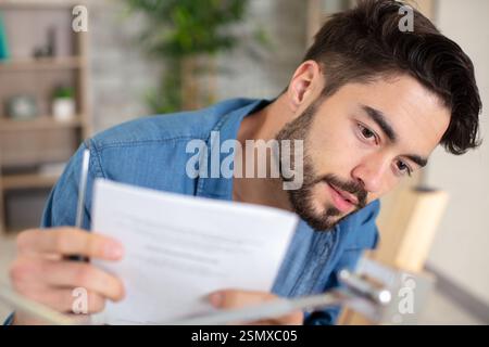 Ein glücklicher junger Geschäftsmann liest Papiere am Schreibtisch im Büro Stockfoto