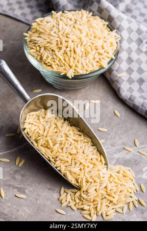 Orzo, Kritharaki, Risoni-Pasta. Ungekochte trockene Nudeln im Löffel auf einem Küchentisch. Stockfoto