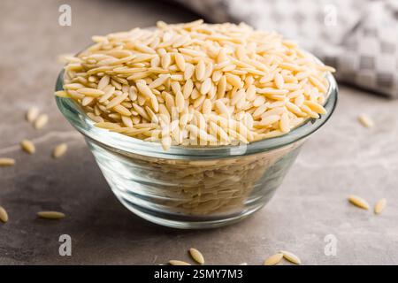 Orzo, Kritharaki, Risoni-Pasta. Ungekochte trockene Nudeln in einer Schüssel auf einem Küchentisch. Stockfoto