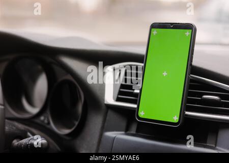 Modell eines Smartphones mit grünem Bildschirm in der Halterung im Auto. Kartennavigator-Anwendung, Transporttechnologie. Stockfoto