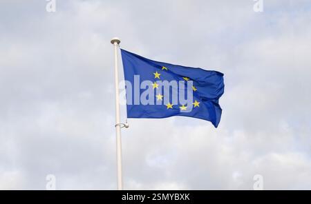 Die Flagge der Europäischen Union winkt im Wind auf dem Fahnenmast gegen den blauen Himmel. Eine europäische Flagge mit zwölf gelben Sternen im Kreis. Stockfoto