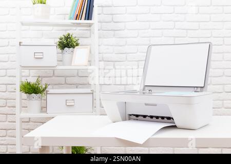Drucken von Dokumenten an einem modernen Arbeitsplatz mit einem eleganten Drucker auf einem weißen Tisch vor einer Ziegelwand Stockfoto
