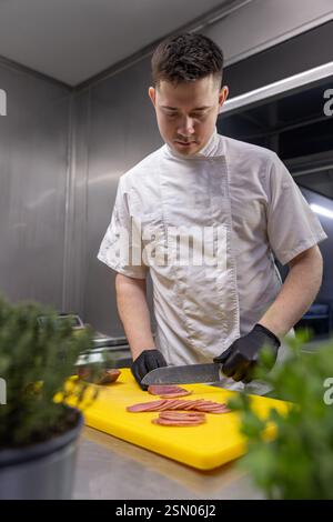 Der Koch trägt schwarze Handschuhe und schneidet gekonnt frischen Thunfisch auf einem leuchtend gelben Schneidebrett Stockfoto