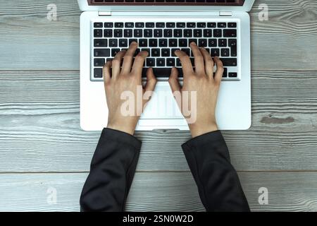 Weibliche Hände, die auf einer Laptop-Tastatur auf einem grauen Holztisch tippen, von oben in einer professionellen Büroumgebung erfasst und das foc hervorheben Stockfoto