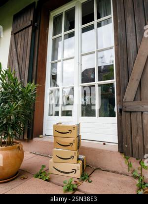 Paris, Frankreich - 20. Oktober 2021: Vier Amazon-Pakete stapelbar auf einer Terrasse vor einer weißen französischen Tür mit Holzläden, neben einem Topf Stockfoto