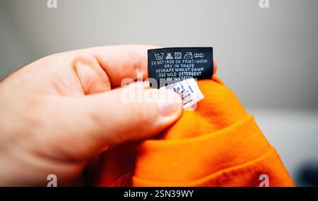 Paris, Frankreich – 26. März 2023: Nahaufnahme einer Hand mit einem Pflegehinweis an einem orangefarbenen Baumwollbekleidung, in dem das Waschen, Trocknen und Bügeln beschrieben ist Stockfoto