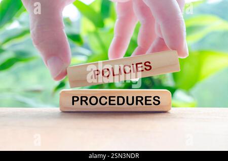 Richtlinien- und Verfahrensvorschriften auf Holzblöcken mit Hand und verschwommenem Hintergrund. Stockfoto