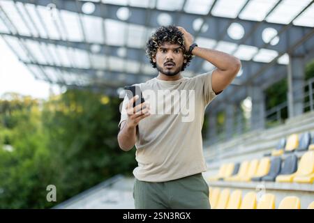 Der Athlet sieht die Kamera verärgert und enttäuscht an. Der Mann hält das Telefon mit der App zur Trainingsverfolgung in der Hand. Stockfoto