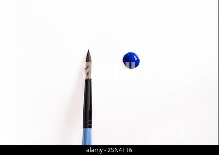 Ein blauer Farbtropfen neben einem sauberen Pinsel auf weißem Hintergrund Stockfoto