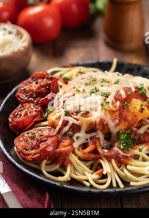Hühnerparmesan mit Spaghettinudeln, Sauce und gebratenen Tomaten, garniert mit Basilikumblättern und gehackter Petersilie auf einem Teller Stockfoto
