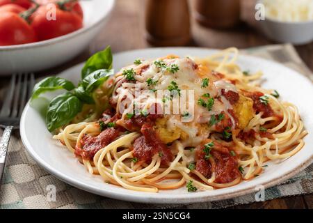 Hühnerparmesan mit Spaghettinudeln und Sauce garniert mit Basilikumblättern und gehackter Petersilie auf einem Teller Stockfoto