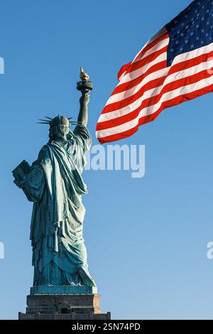 Eine Nahaufnahme der Freiheitsstatue, die lebendigen Patriotismus unter amerikanischer Flagge ausstrahlt, vom Fuße von Liberty Island, New York City. Stockfoto