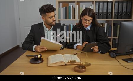 Mann und Frau arbeiten zusammen in einem Büro mit Rechtsbüchern, Waagen und einem Hammer, wobei sie die Zusammenarbeit in einem professionellen juristischen umfeld demonstrieren Stockfoto