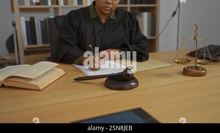 Frau Richterin schreibt Notizen am Schreibtisch im Gerichtssaal mit Gesetzbüchern, Hameln und Waagen Stockfoto