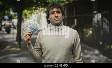 Hispanischer Mann, der polnische Zloty-Banknoten auf einer Stadtstraße hält, Geldwechsel oder persönliche Finanzen in einem urbanen Außenbereich präsentiert. Stockfoto