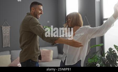 Glückliches Paar tanzt zusammen in einem gemütlichen Wohnzimmer voller Pflanzen und unterstreicht ihre fröhliche Beziehung und ihre schöne Bindung zu Hause. Stockfoto