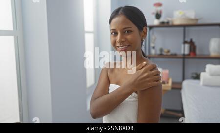 Wunderschöne hispanische Frau berührte die Schulter im Spa-Wellnessraum, lächelte und in Handtuch gewickelt Stockfoto