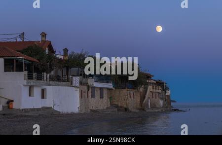 Ein Mond scheint auf dem Wasser in der Nähe eines Strandes. Der Mond ist der Hauptfokus des Bildes Stockfoto