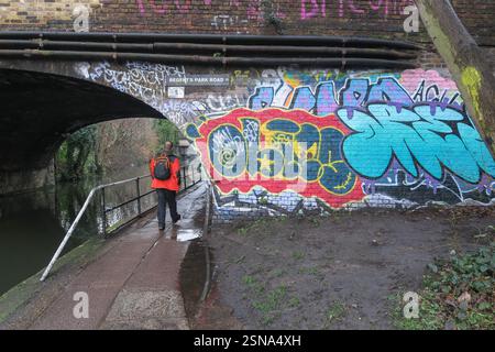 Mann, der unter einer Brücke läuft, die mit Graffiti bedeckt ist, an der Regents Park Road am Regents Canal Stockfoto
