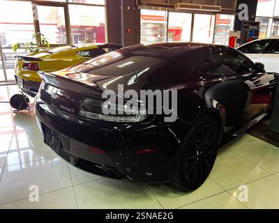 Lviv, Ukraine - 12. Februar 2025: Der glänzend schwarze Sportwagen Aston Martin Vantage S parkt im Innenbereich unter hellen Lichtern mit moderner Architektur. Stockfoto
