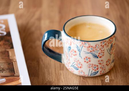 Bristol, Großbritannien. Eine Tasse heißer Kaffee, serviert in einem porzellanbecher. Das Getränk wird im Becher auf einem einfachen Tisch neben einem Magazin serviert Stockfoto