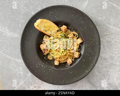 Pasta Spaghetti Hähnchenpilz mit Trüffelsauce, gewürztem Schnittlauchschnitt und italienischen Kräutern, serviert mit Knoblauchbrot auf schwarzem Teller, auf grauem Marmor Stockfoto
