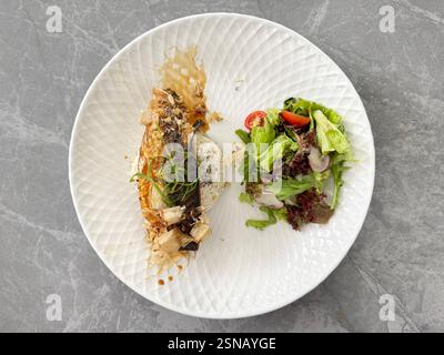 Gegrillte Fischmakrele mit gewürztem Reis und Caesar-Salat. Serviert auf einem weißen runden Teller, auf grauem Marmortisch. Stockfoto