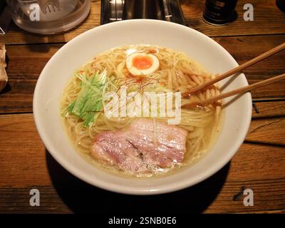 Eine Dampfschale mit köstlichen Ramen steht auf einem rustikalen Holztisch, gefüllt mit Nudeln, Brühe und Belägen. Stockfoto