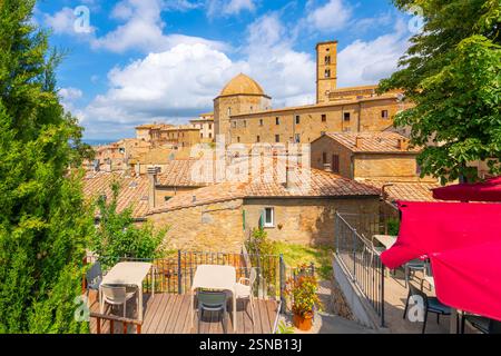 Ein kleines Café im Freien mit Blick auf die mittelalterliche Bergstadt Volterra, Italien, in der toskanischen Landschaft. Stockfoto