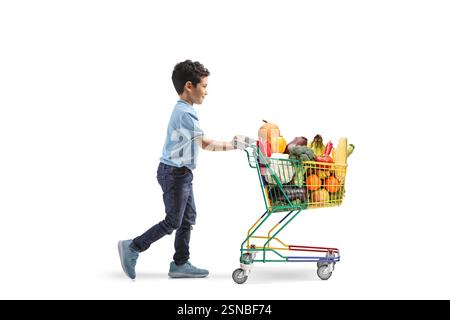 Profilaufnahme eines Kindes in voller Länge, das einen Einkaufswagen mit Obst und Gemüse auf weißem Hintergrund läuft und schiebt Stockfoto