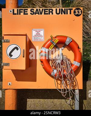 Eine orangefarbene britische Küsten-Notfallstation mit einer Lebensretter-Einheit, einem Notruftelefon, einem roten Rettungsring und einer Wurfleine Stockfoto