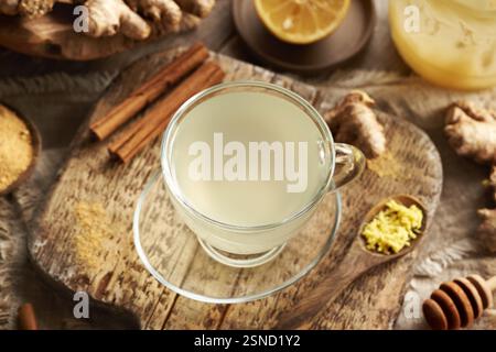 Eine Tasse Kräutertee aus frischer Ingwerwurzel mit Zimt, Zitrone und Honig auf einem Holztisch Stockfoto