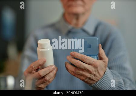 Nahaufnahme der Hände eines älteren männlichen Patienten mit einer leeren weißen Plastikflasche und einem Pillenbehälter mit verschriebenen Medikamenten, Behandlungskonzept zu Hause, Kopierraum Stockfoto