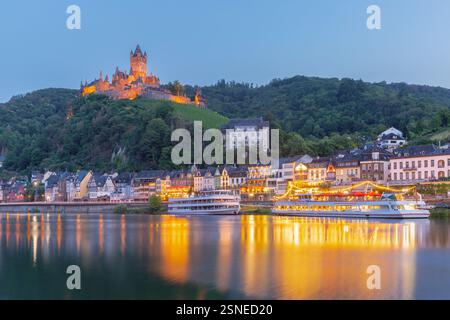 Abendlicher Blick auf Cochem, mit beleuchteten Booten auf der Mosel, die den farbenfrohen Sonnenuntergang reflektieren, Deutschland Stockfoto