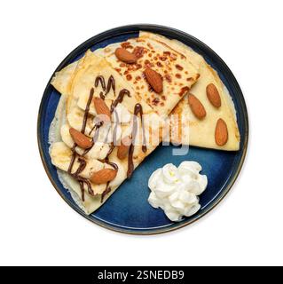 Köstliche Crepes mit Schokoladensauce, Banane, Mandeln und Schlagsahne isoliert auf weiß, Blick von oben Stockfoto