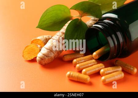 Kurkuma-Rhizome, Kapseln und umgedrehte medizinische Flasche auf orangem Hintergrund, Nahaufnahme Stockfoto