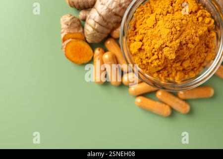 Kurkumapulver in Schüssel, Wurzeln und Kapseln auf grünem Hintergrund, flach gelegt. Leerzeichen für Text Stockfoto