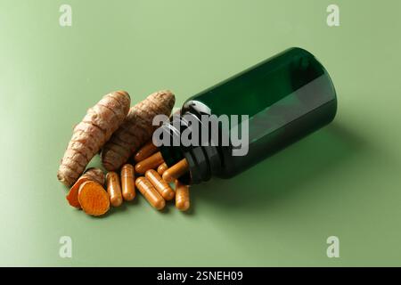 Kurkuma Kapseln, Wurzeln und umgedrehte medizinische Flasche auf grünem Hintergrund Stockfoto